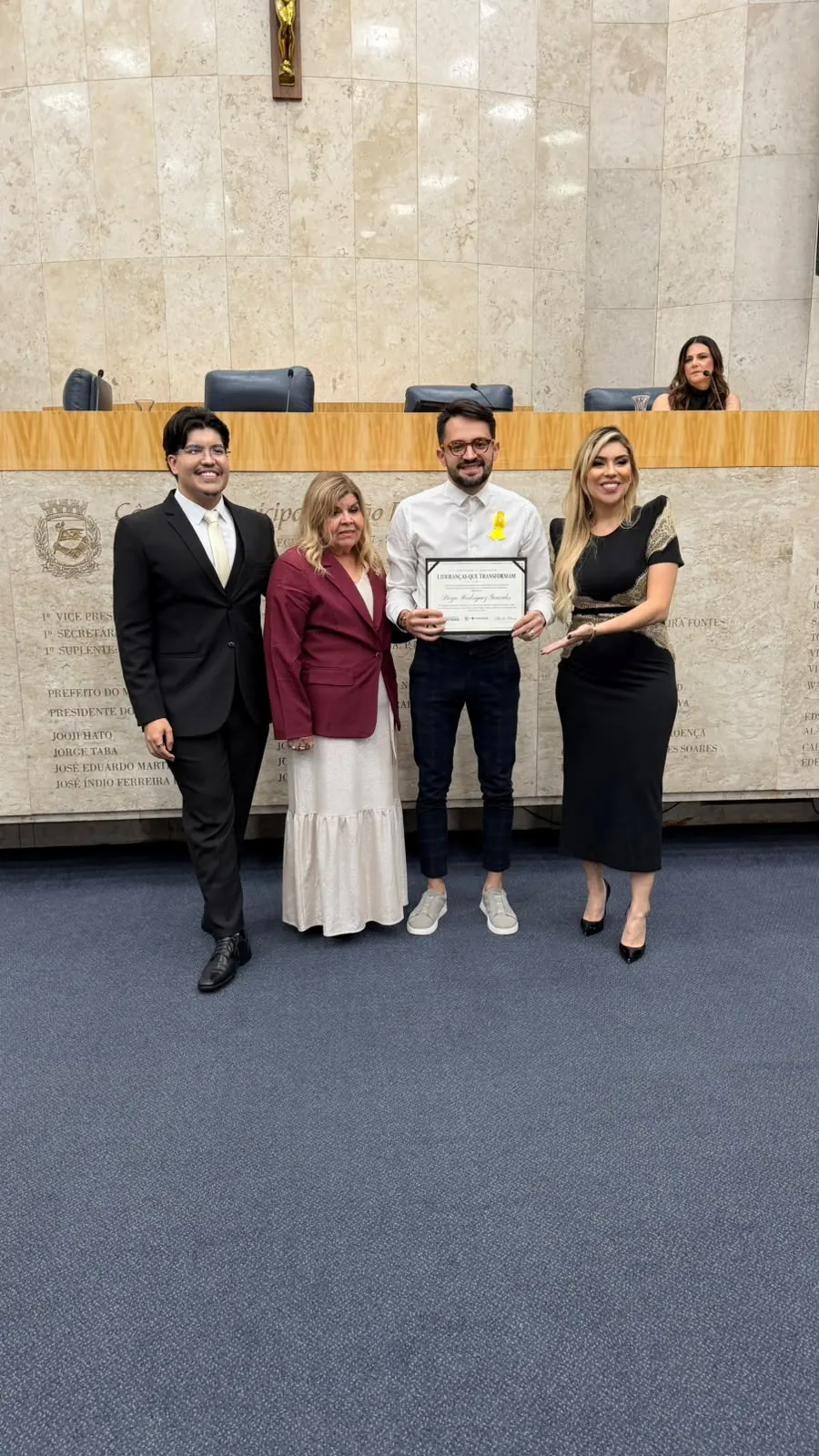 Registro da entrega da homenagem, com o certificado e os participantes da cerimônia